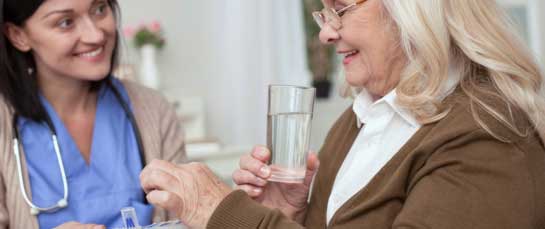 Positive mature woman taking pills from nurse while looking down
